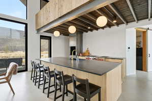 Open-concept kitchen featuring an expansive island with a dark countertop, light wood-finish cabinetry, and a professional-grade range