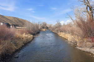 Riverfront property featuring natural waterside vegetation, a clear flowing river, and a distant building with a dark roofline