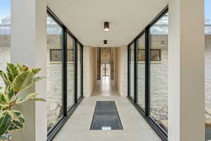 Corridor featuring floor-to-ceiling windows, exposed stone walls, concrete flooring, and recessed ceiling lighting