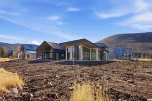 Contemporary-style residence featuring a dark metal roof, expansive glass windows, light-colored stone accents, a covered patio, and a sloped roofline
