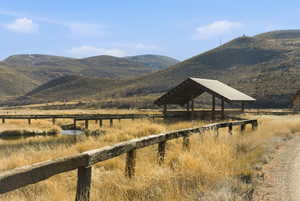 Expansive natural landscape featuring a wooden shelter with a peaked roof, a winding boardwalk over a water feature, and a rustic wooden fence line