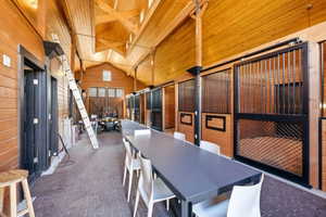 Spacious interior with vaulted wood-plank ceilings, exposed wood beams, and multiple horse stalls featuring black metal gates