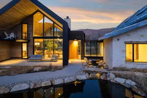 Modern architectural residence featuring a prominent A-frame structure with expansive glass, a stone-clad wing, and a connecting glass-enclosed walkway