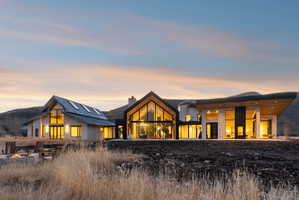 Contemporary architectural design featuring diverse building materials, expansive full-height windows, a prominent gable roofline, and an outdoor fire pit area