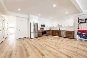 Two tone kitchen featuring stainless steel appliances, light wood-style floors, light countertops, recessed lighting, and two tone color scheme