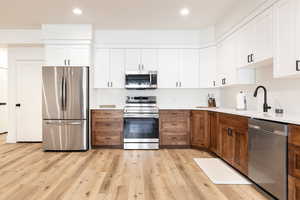 Dual tone kitchen with stainless steel appliances, dual tone cabinetry, light wood-style floors, recessed lighting, and light stone counters