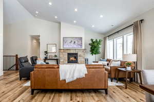Living area with lofted ceiling, light wood-style flooring, a stone fireplace, and recessed lighting
