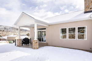 Snow covered property with a patio area, stucco siding, and a mountain view
