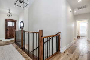 Hallway with light wood-type flooring, an upstairs landing, lofted ceiling, and recessed lighting