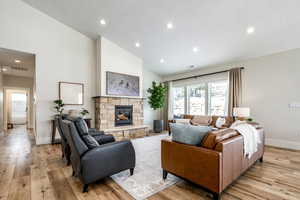 Living area with light wood-style floors, vaulted ceiling, a stone fireplace, and recessed lighting