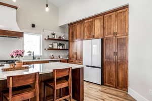 Kitchen featuring freestanding refrigerator, light wood-style flooring, open shelves, a kitchen bar, and light stone countertops