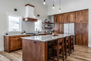 Kitchen with a kitchen island, light wood-type flooring, a kitchen breakfast bar, a high ceiling, and open shelves