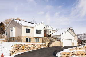 View of front facade featuring stone siding, a balcony, an attached garage, and asphalt driveway