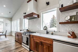 Kitchen featuring decorative backsplash, stainless steel appliances, lofted ceiling, open shelves, and light wood finished floors