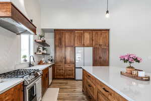 Kitchen with stainless steel gas range oven, wood finish cabinets, freestanding refrigerator, light wood-type flooring, and tasteful backsplash
