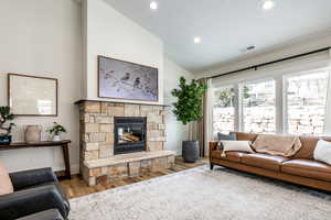 Living room featuring vaulted ceiling, a stone fireplace, wood finished floors, and recessed lighting