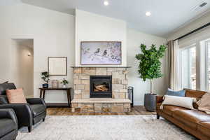 Living area featuring lofted ceiling, wood finished floors, a stone fireplace, and recessed lighting