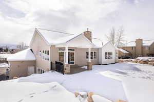 Snow covered back of property featuring a patio, a chimney, and stucco siding