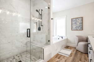 Full bath with vanity, a marble finish shower, a garden tub, and light wood-style floors