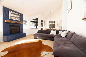 Living room with light wood-style floors, vaulted ceiling, and a brick fireplace
