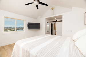 Bedroom with wood finished floors, a barn door, a ceiling fan, and ensuite bathroom