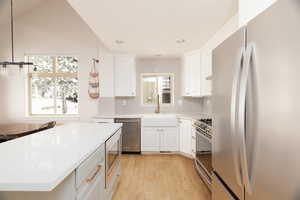 Kitchen featuring stainless steel appliances, light wood-style floors, white cabinets, tasteful backsplash, and a center island