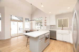 Kitchen featuring lofted ceiling, hanging light fixtures, stainless steel appliances, a kitchen breakfast bar, and light wood-type flooring
