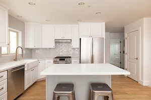 Kitchen with stainless steel appliances, light wood-style floors, a center island, a breakfast bar, and recessed lighting