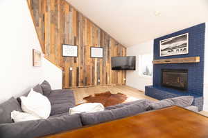 Living room with wooden walls, wood finished floors, lofted ceiling, a fireplace, and an accent wall