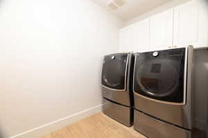 Laundry area with cabinet space, separate washer and dryer, and light wood-style flooring