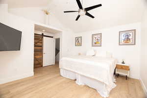Bedroom with a barn door, light wood-style floors, a ceiling fan, and a high ceiling