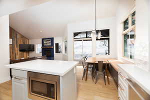 Kitchen with a brick fireplace, stainless steel microwave, lofted ceiling, light countertops, and a kitchen island