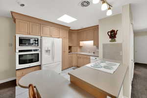 Kitchen featuring light countertops, white appliances, tasteful backsplash, light wood finish cabinetry, and light tile patterned floors