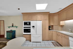 Kitchen with light wood finish cabinets, white appliances, light tile patterned flooring, and backsplash
