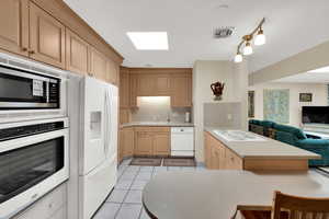 Kitchen with white appliances, light countertops, open floor plan, light wood finish cabinetry, and tasteful backsplash