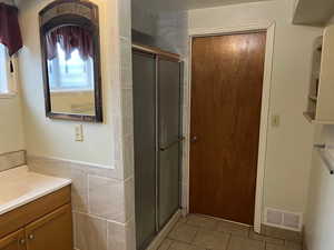 Basement bathroom featuring a shower stall, vanity, light tile patterned floors, and tile walls