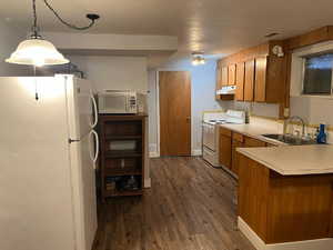 Basment Kitchen featuring wood finish cabinets, white appliances, light countertops, dark wood-style floors, and pendant lighting