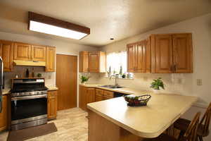 Kitchen with stainless steel range with gas stovetop, light countertops, wood finish cabinets, a peninsula, and a textured ceiling