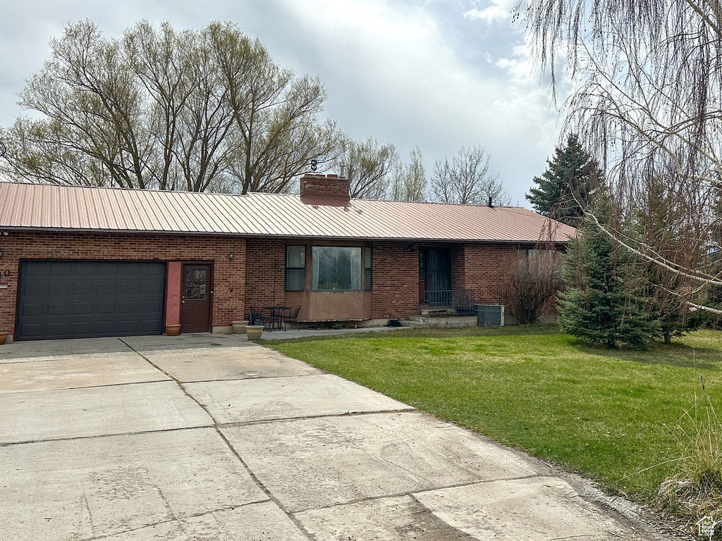 Ranch-style house with concrete driveway, a metal roof, a front yard, brick siding, and a garage