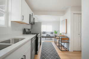 Kitchen with stainless steel appliances, white cabinetry, light stone counters, and light wood-style flooring