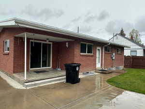Brick exterior featuring a covered patio with concrete steps, sliding glass door, multiple windows, and a manicured lawn