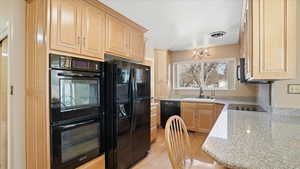 Kitchen with black appliances, light stone counters, light wood finish cabinets, and light wood-style flooring