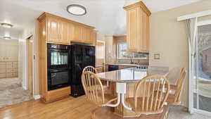 Kitchen with light wood finish cabinets, black appliances, light stone counters, a peninsula, and a kitchen breakfast bar