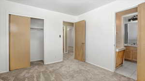Unfurnished bedroom featuring light carpet, a closet, and ensuite bath