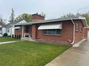 Brick exterior residence featuring a front porch, white striped awnings, a paved driveway, and a manicured lawn
