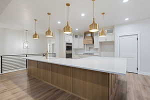 Kitchen with glass insert cabinets, two tone color scheme, light wood-type flooring, light stone counters, and tasteful backsplash