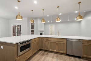 Kitchen featuring stainless steel appliances, hanging light fixtures, light wood finished floors, wood finish cabinetry, and light stone counters