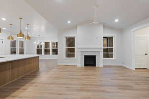 Unfurnished living room featuring lofted ceiling, light wood finished floors, a fireplace, and suspended lighting