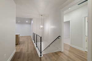 Hallway with an upstairs landing, light wood finished floors, and a chandelier