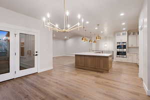Two tone kitchen featuring glass insert cabinets, a large island, a chandelier, open floor plan, and dual tone cabinetry